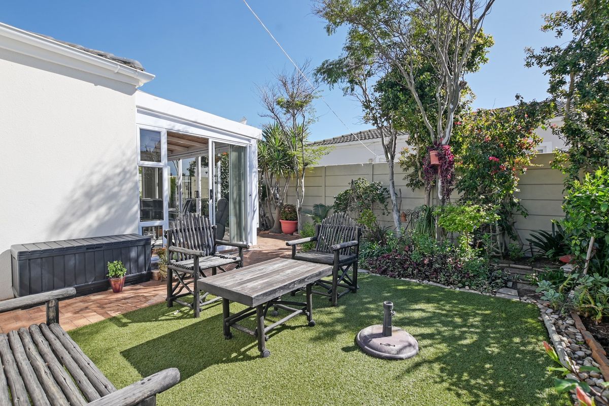 A private rear garden featuring a paved patio area, artificial lawn, and direct access to the home through sliding glass doors.