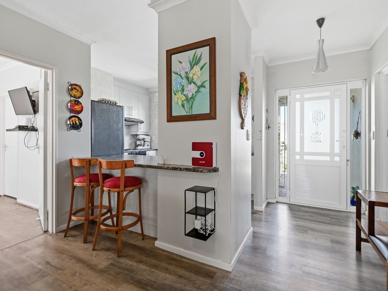 Open plan living area featuring a breakfast bar, modern laminate flooring, and a bright entrance with a decorative glass panel door.