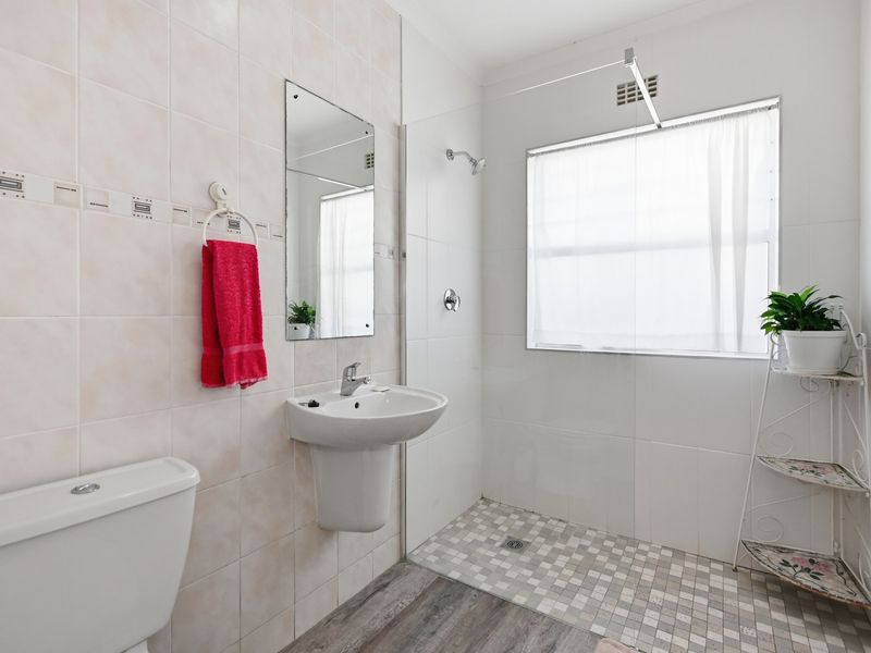 A functional bathroom featuring a pedestal washbasin, walk-in shower with tiled flooring, and neutral wall tiling.