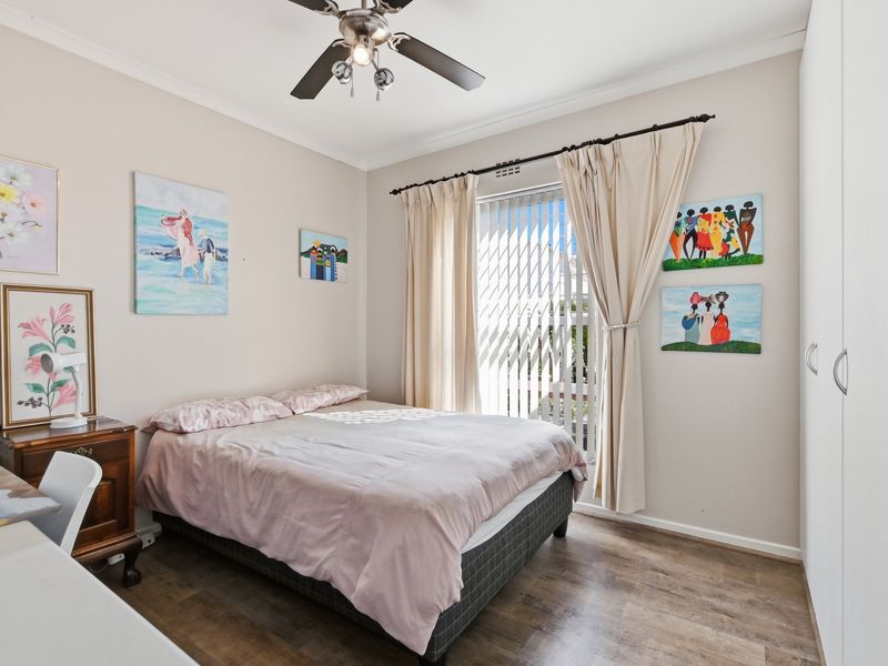 A well-maintained bedroom featuring laminate flooring, a ceiling fan, and built-in wardrobe storage with natural light from the window.
