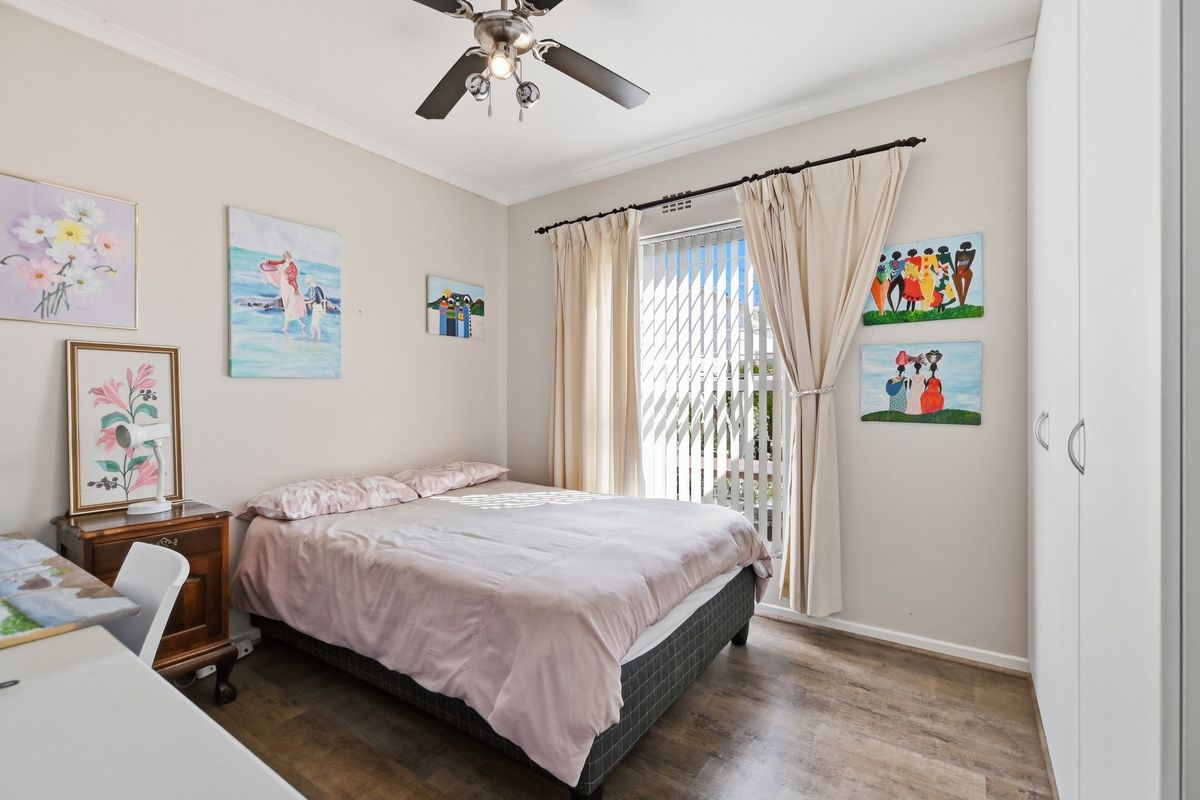 A well-maintained bedroom featuring laminate flooring, a ceiling fan, and built-in wardrobe storage with natural light from the window.