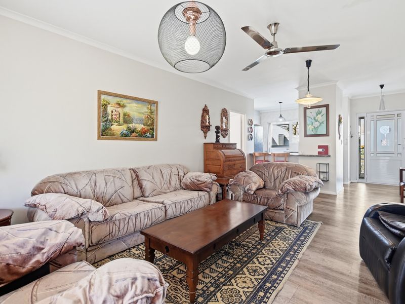 Open plan living area featuring laminate flooring, ceiling fan, and a breakfast bar connecting to the kitchen space.