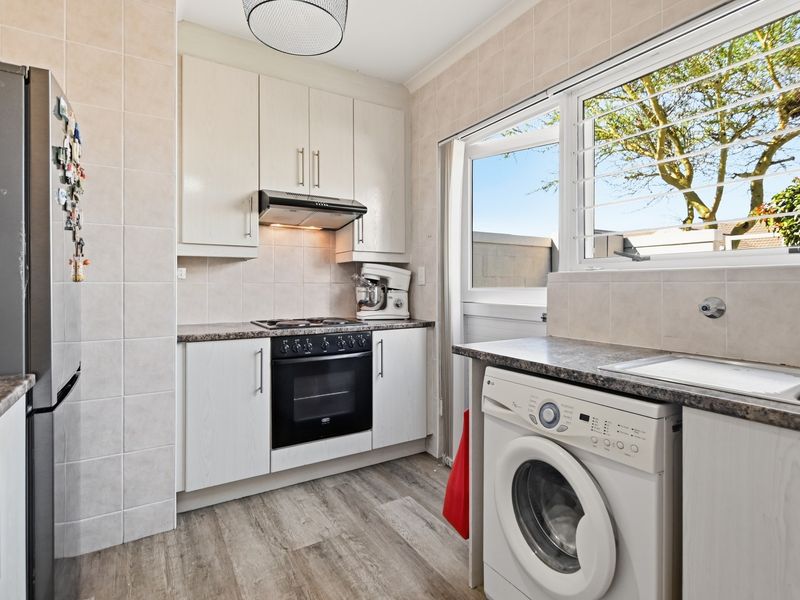 Compact kitchen featuring built-in cabinetry, laminate countertops, integrated oven and hob, and a dedicated space for laundry appliances.