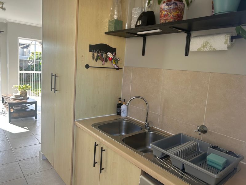 A functional scullery area featuring light wood-look cabinetry, a double stainless steel sink, and tiled splashback, with direct access to an outdoor patio.