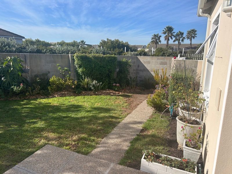 A private rear garden featuring a lawn, paved walkway, and established garden beds enclosed by a concrete boundary wall.