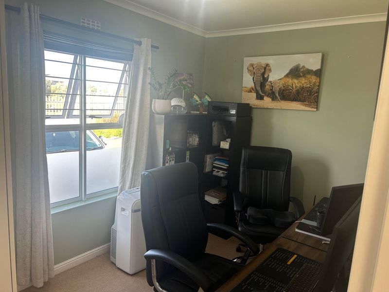 A functional home office space featuring carpeted flooring, a window with security bars, and neutral wall tones.