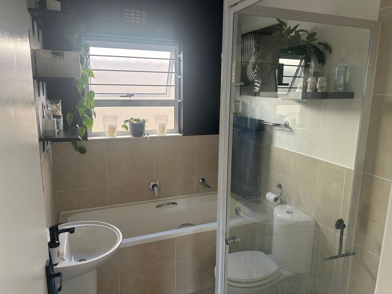 A functional bathroom featuring a pedestal basin, built-in bathtub, separate shower enclosure, and toilet with neutral wall tiling.