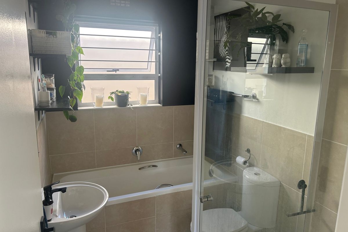 A functional bathroom featuring a pedestal basin, built-in bathtub, separate shower enclosure, and toilet with neutral wall tiling.