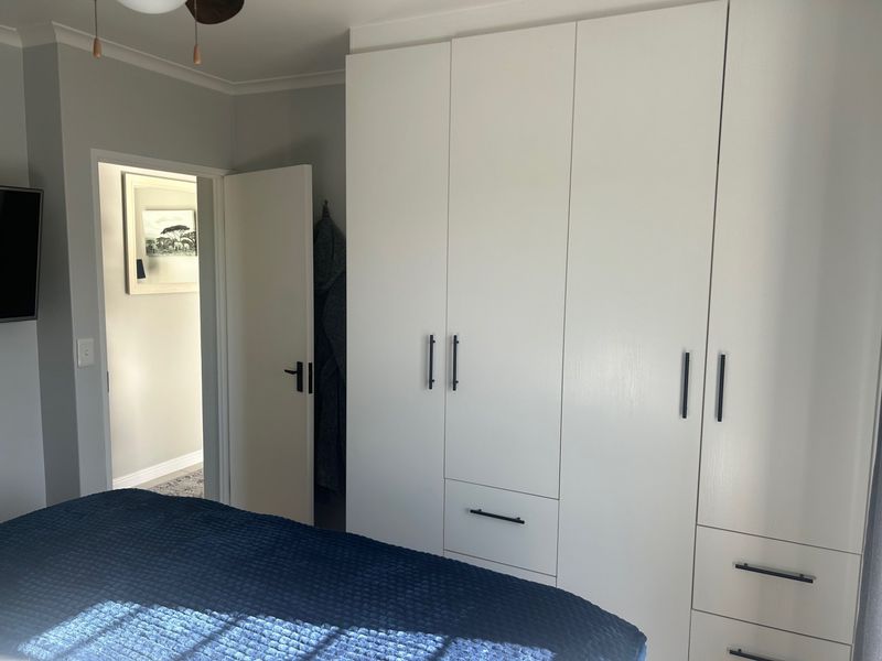 A well-maintained bedroom featuring a large white built-in wardrobe with modern black hardware and a ceiling fan.