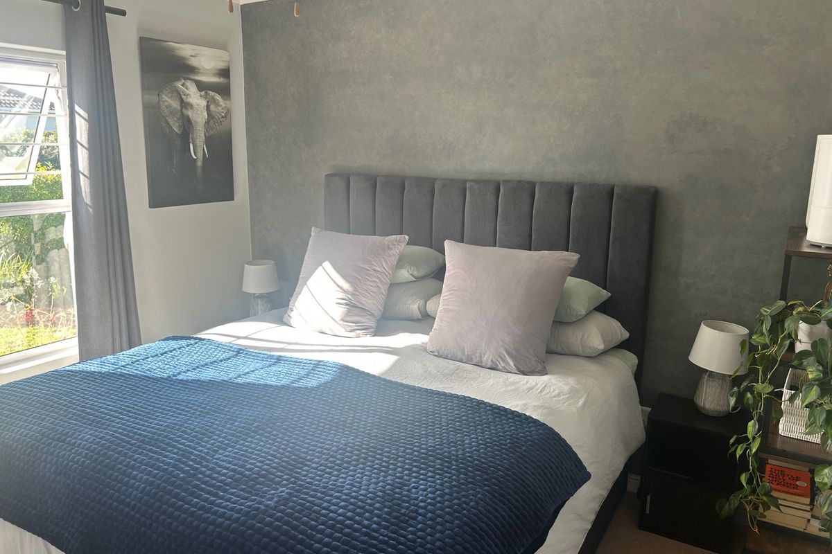 A well-maintained bedroom featuring a textured grey accent wall, a louver window for natural ventilation, and a ceiling fan.