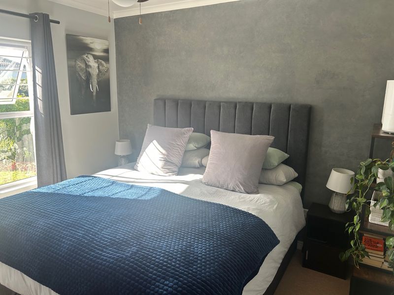 A well-maintained bedroom featuring a textured grey accent wall, a louver window for natural ventilation, and a ceiling fan.