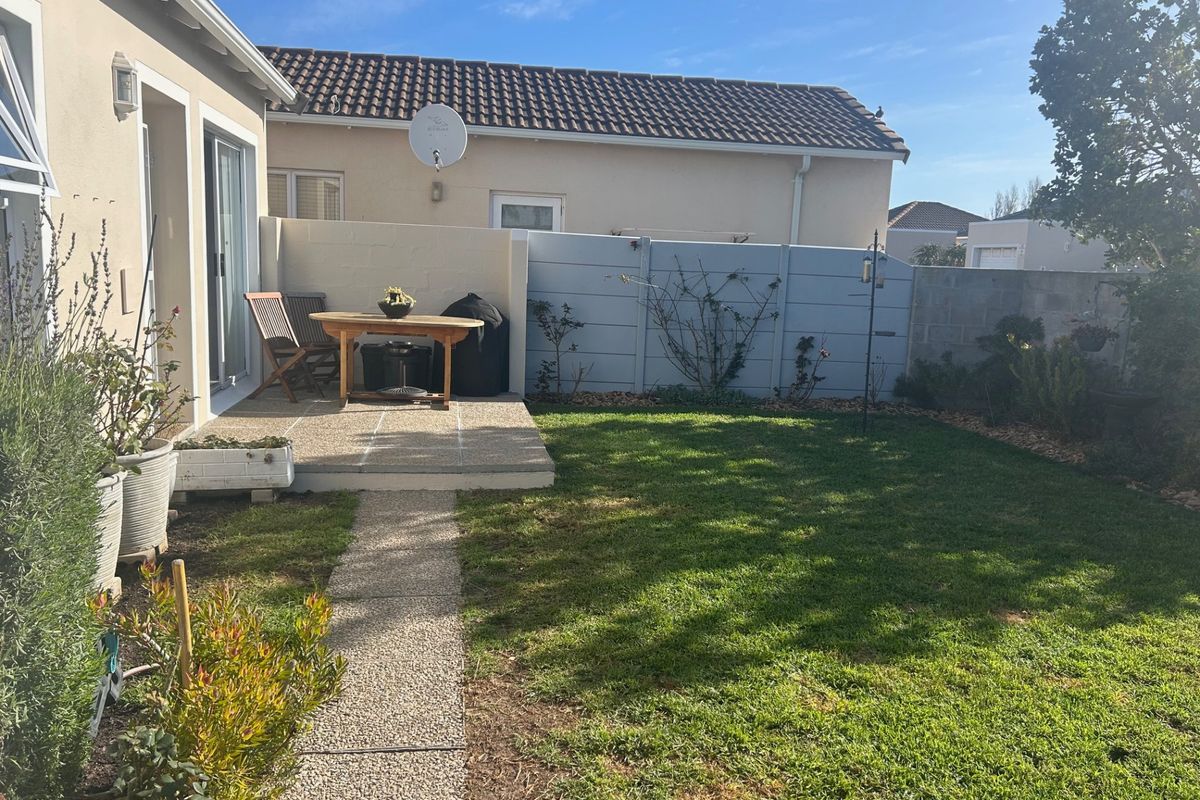 A private rear garden featuring a concrete patio area, a paved pathway, and a well-maintained lawn enclosed by boundary walls.