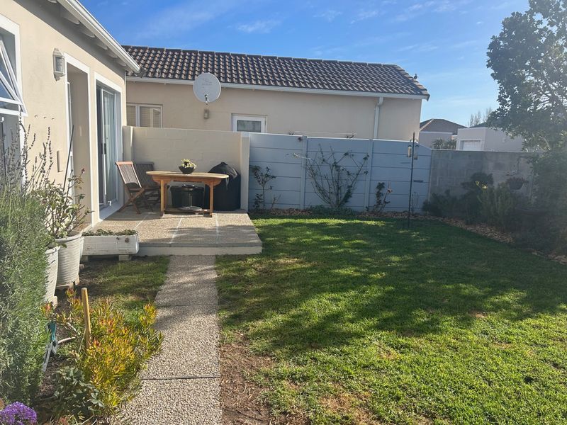 A private rear garden featuring a concrete patio area, a paved pathway, and a well-maintained lawn enclosed by boundary walls.
