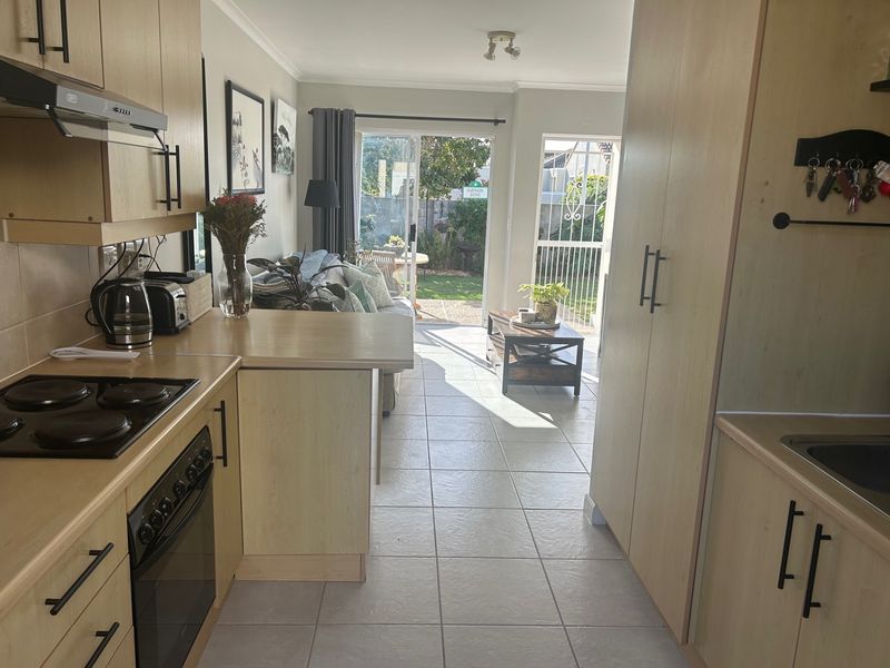 Open-plan kitchen and living area featuring light wood cabinetry, tiled flooring, and direct access to the rear garden through a sliding glass door.