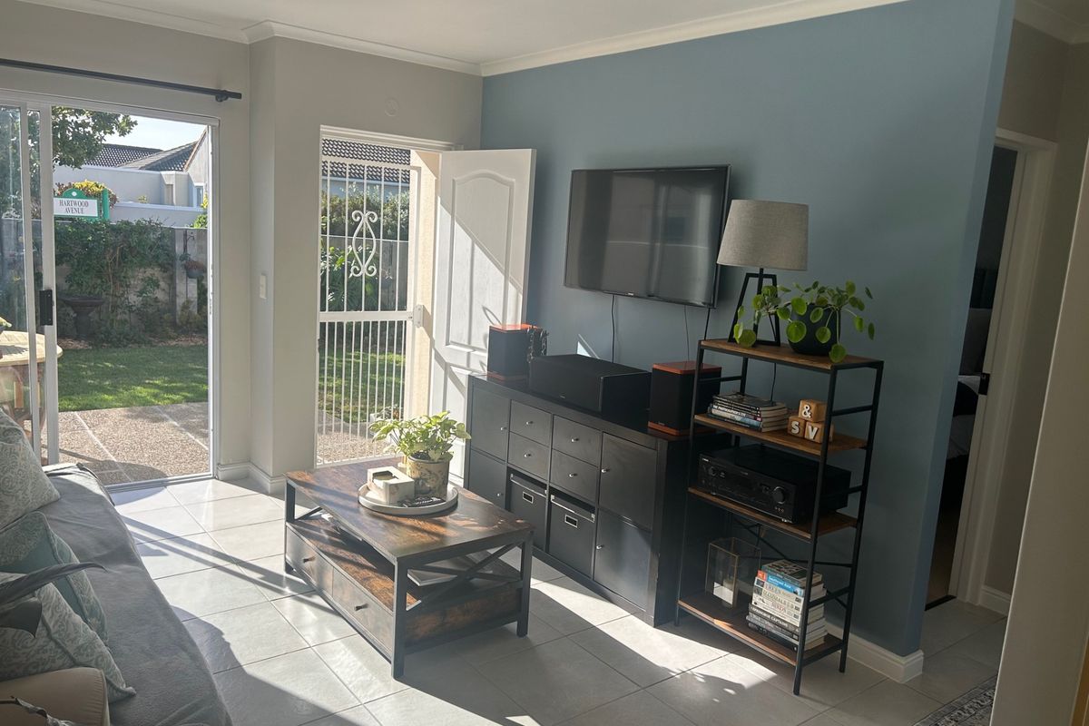 A bright living room featuring tiled flooring, a wall-mounted television, and direct access to the rear garden through a sliding glass door.
