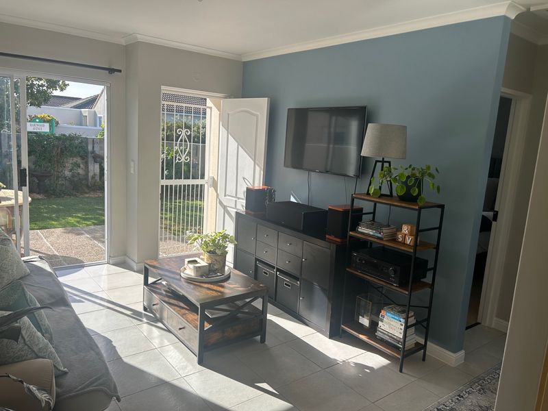 A bright living room featuring tiled flooring, a wall-mounted television, and direct access to the rear garden through a sliding glass door.