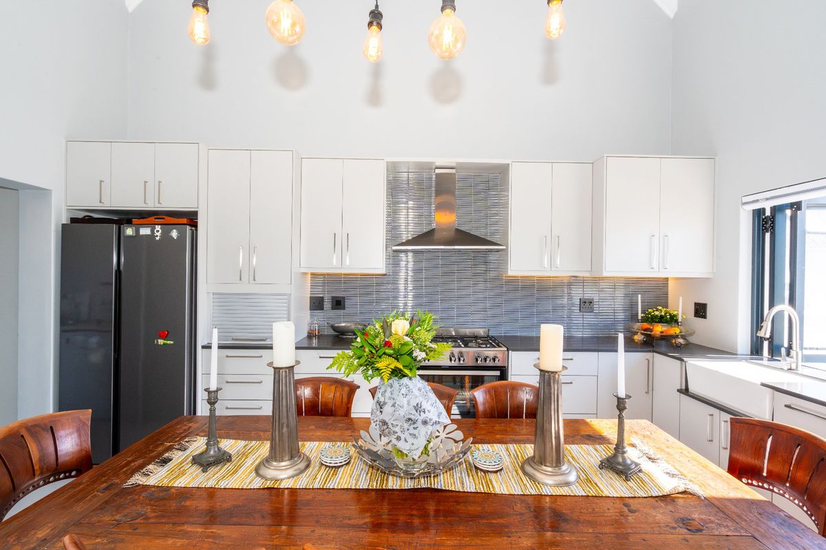 Modern kitchen featuring white cabinetry, stainless steel appliances, a tiled backsplash, farmhouse sink, and vaulted ceilings with stylish pendant lighting.