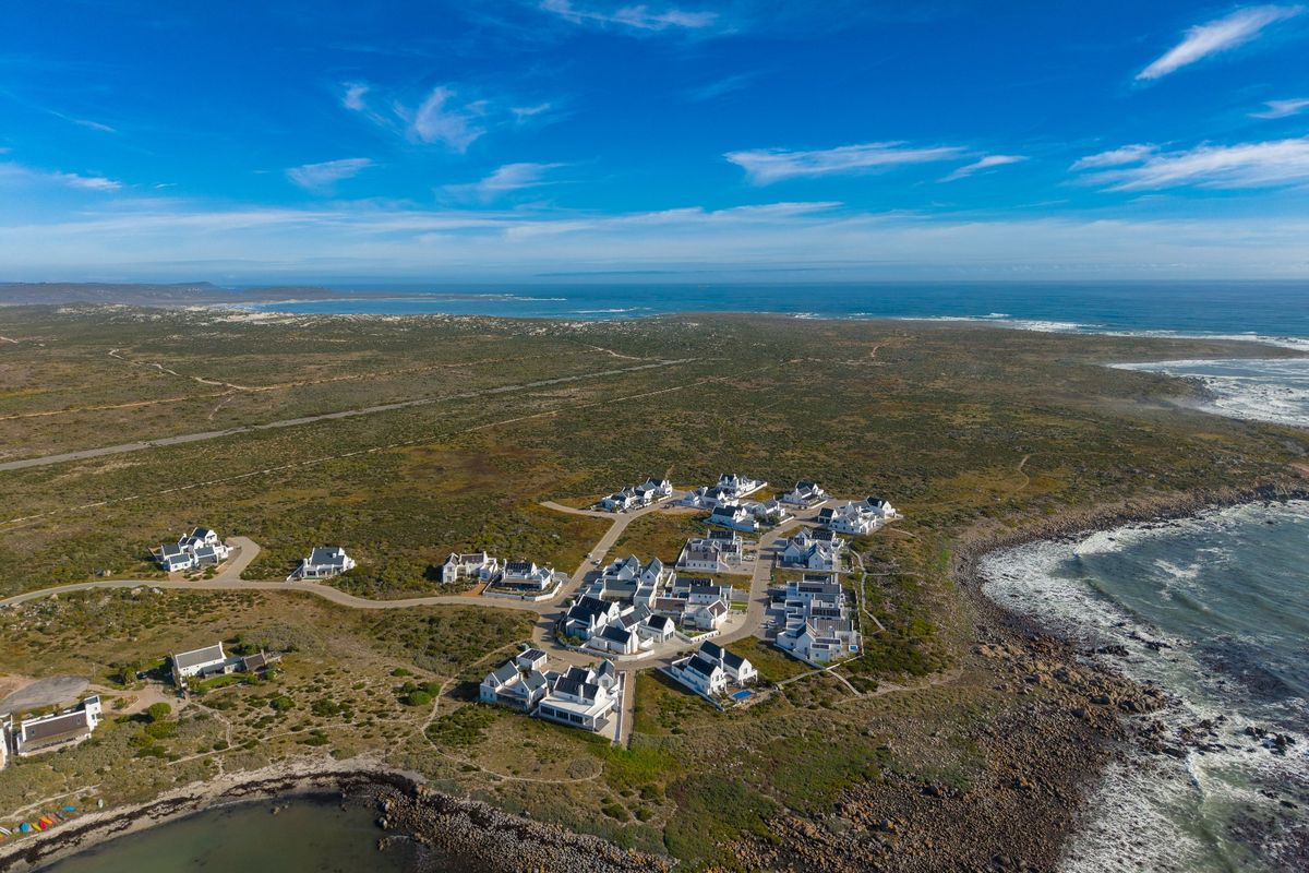 An aerial view of a coastal residential estate situated along the shoreline, showcasing the layout of the properties and surrounding natural landscape.