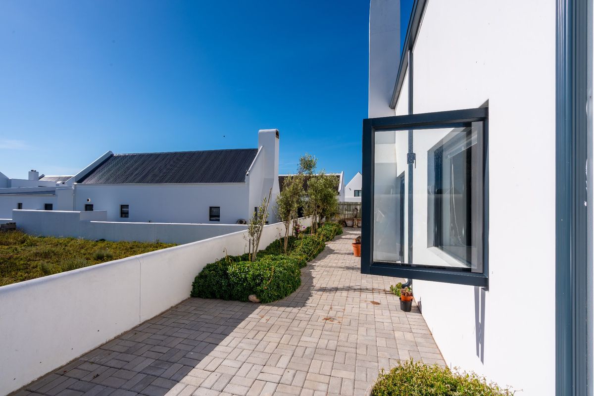A well-maintained paved rear walkway featuring a clean white exterior wall, modern casement window, and a low boundary wall.