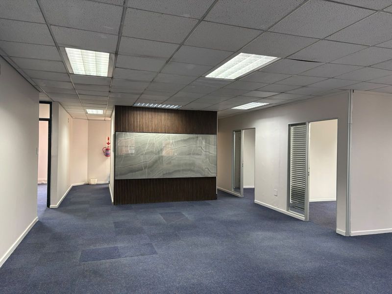 Open plan commercial office space featuring a modern timber slat and stone feature wall, suspended ceiling, and blue carpet tiles.