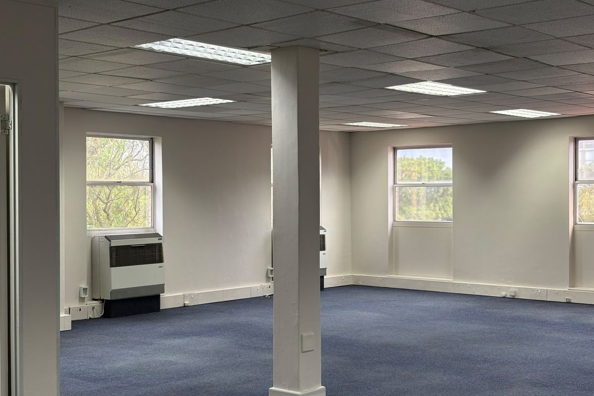 Open-plan commercial office space featuring a suspended ceiling, recessed lighting, wall-mounted air conditioning units, and carpeted flooring.