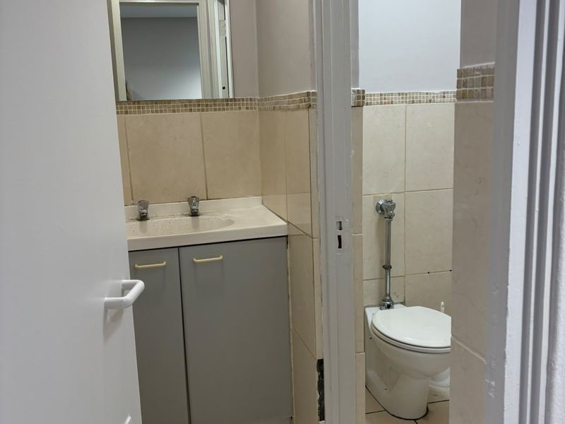 A functional commercial bathroom featuring a vanity with basin, wall mirror, and a separate toilet cubicle with tiled finishes throughout.