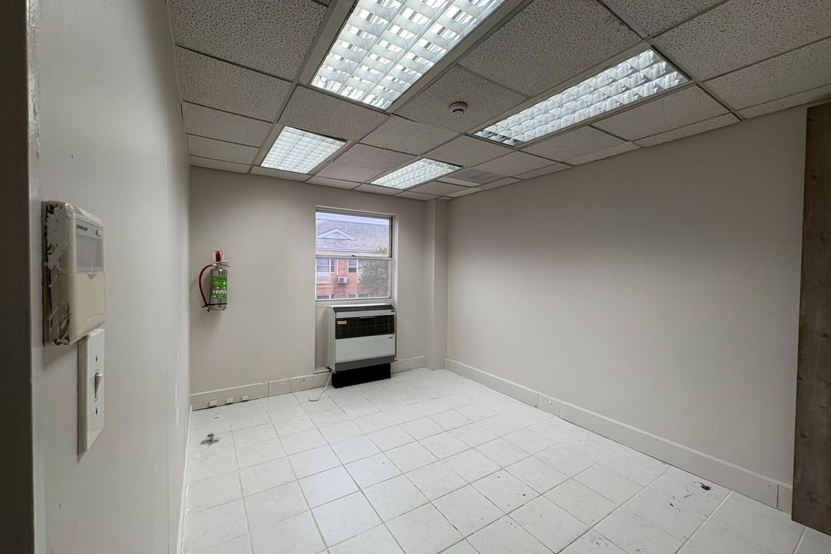 A vacant commercial office space featuring tiled flooring, a suspended ceiling with recessed lighting, and a built-in PTAC air conditioning unit.