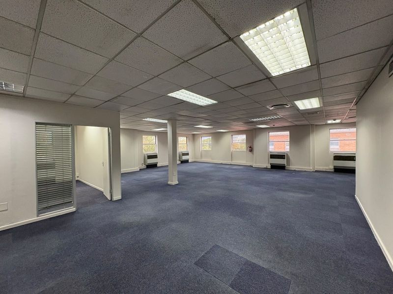 Spacious open-plan commercial office area featuring suspended ceilings, recessed lighting, carpeted flooring, and multiple wall-mounted air conditioning units.