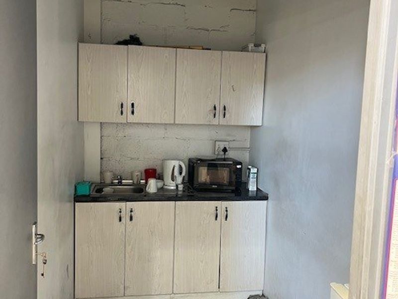 A compact kitchenette featuring built-in cabinetry, a stainless steel sink, and exposed industrial-style wall and ceiling finishes.