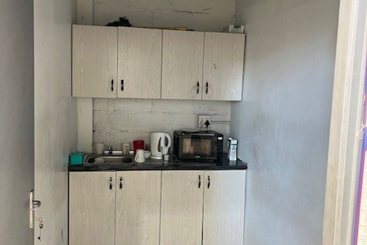 A compact kitchenette featuring built-in cabinetry, a stainless steel sink, and exposed industrial-style wall and ceiling finishes.