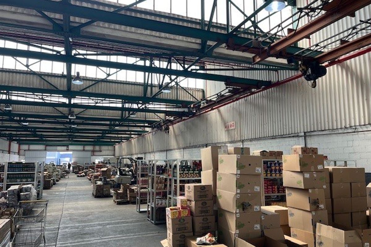 Large industrial warehouse space featuring high ceilings with exposed steel trusses, overhead crane infrastructure, and durable concrete flooring.