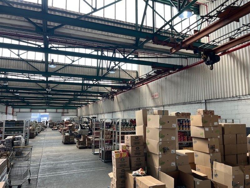 Large industrial warehouse space featuring high ceilings with exposed steel trusses, overhead crane infrastructure, and durable concrete flooring.