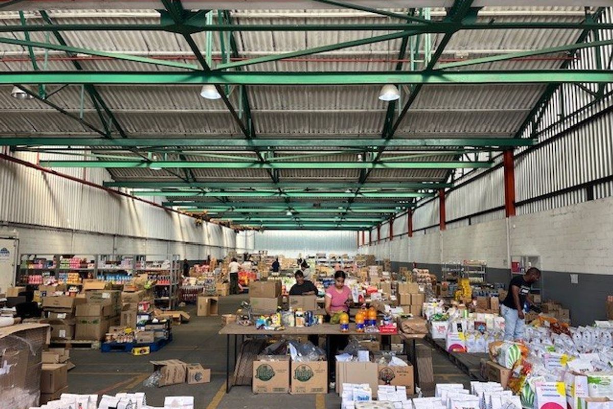 Large industrial warehouse space featuring high exposed steel roof trusses, concrete flooring, and functional masonry walls, currently utilized for storage and distribution operations.