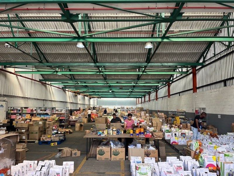 Large industrial warehouse space featuring high exposed steel roof trusses, concrete flooring, and functional masonry walls, currently utilized for storage and distribution operations.