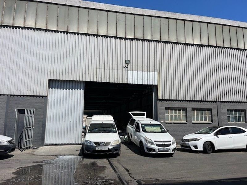 Commercial industrial warehouse exterior featuring corrugated metal cladding, a large roller shutter door, and brick masonry facade with clerestory windows.