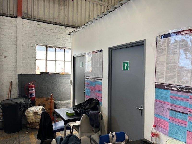 Utility area within a commercial warehouse space featuring exposed brick walls, industrial windows, and access doors to restroom facilities.