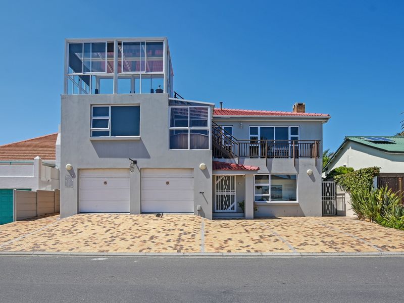 Front elevation of a multi-level house featuring a double garage, paved driveway, and an upper-level balcony with a tiled roof.