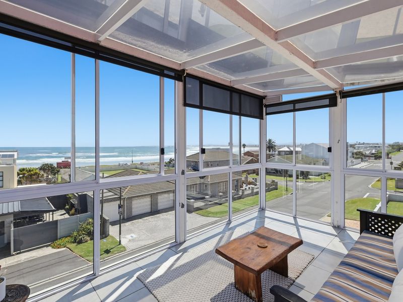 An enclosed sunroom or balcony featuring tiled floors and expansive glass windows offering panoramic coastal and neighbourhood views.