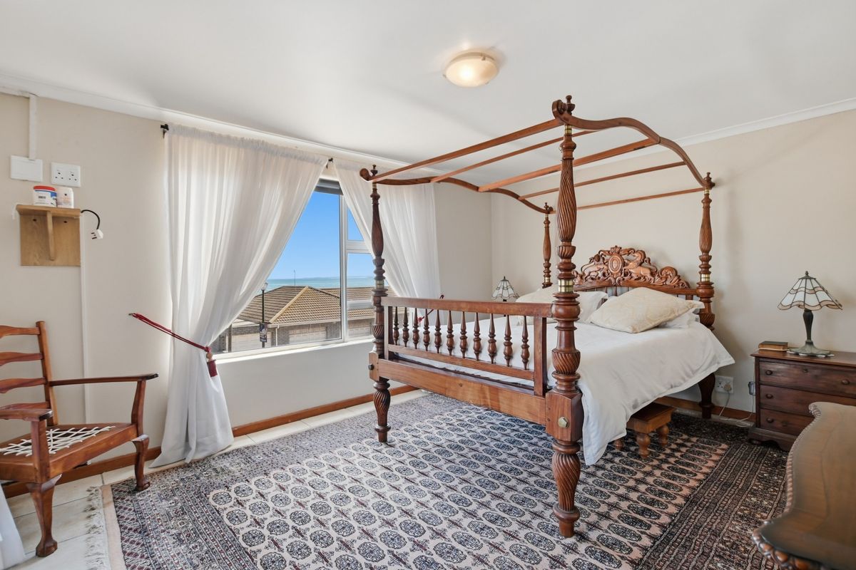 A well-lit bedroom featuring a large window with coastal views, neutral wall finishes, and tiled flooring.