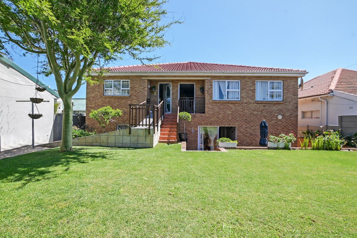 Rear view of a double-story brick house featuring a raised wooden deck, staircase, and a well-maintained garden lawn.