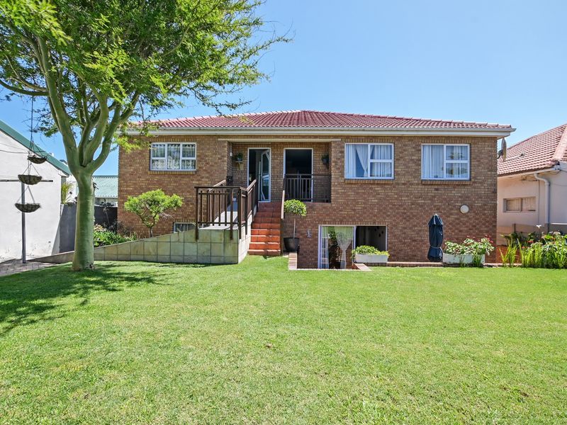Rear view of a double-story brick house featuring a raised wooden deck, staircase, and a well-maintained garden lawn.