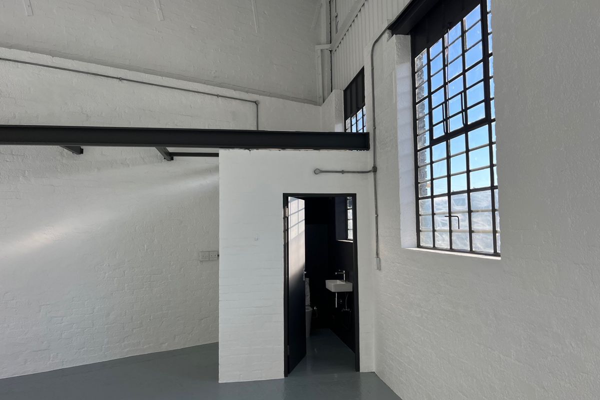 Spacious industrial-style open plan area featuring high ceilings, exposed steel beams, large steel-framed windows, and polished epoxy flooring with an integrated bathroom.