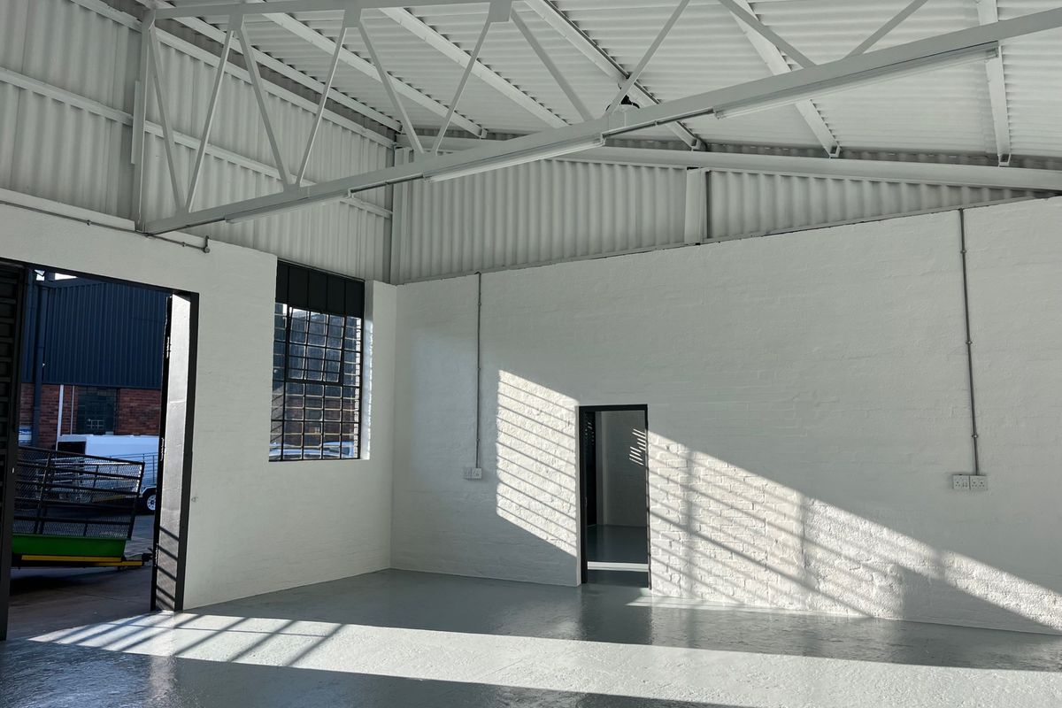 A clean, industrial-style commercial utility space featuring high ceilings with exposed steel trusses, painted brick walls, and durable epoxy-coated concrete flooring.