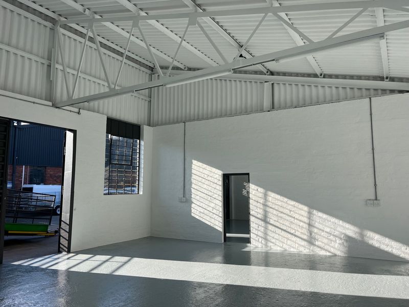 A clean, industrial-style commercial utility space featuring high ceilings with exposed steel trusses, painted brick walls, and durable epoxy-coated concrete flooring.