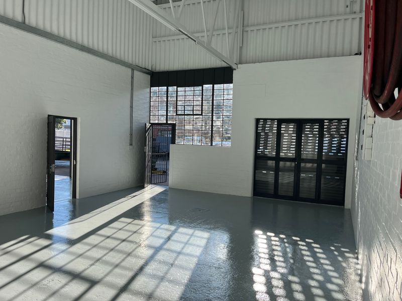 Spacious industrial utility area featuring high ceilings with exposed steel trusses, polished epoxy flooring, and large steel-framed windows providing ample natural light.