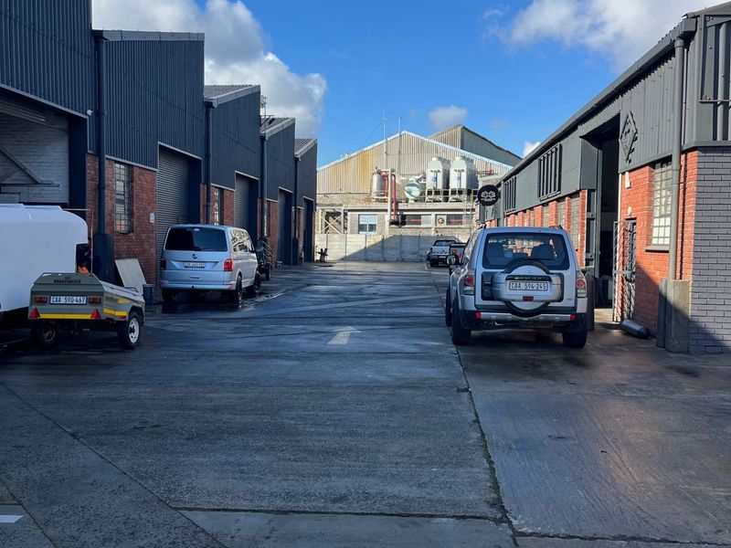 Commercial exterior view showing a concrete driveway between two industrial warehouse buildings with brick and corrugated metal facades.