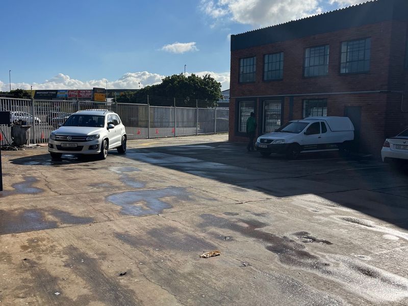 Commercial property exterior featuring a brick facade with industrial windows and a large concrete paved yard area with perimeter security fencing.