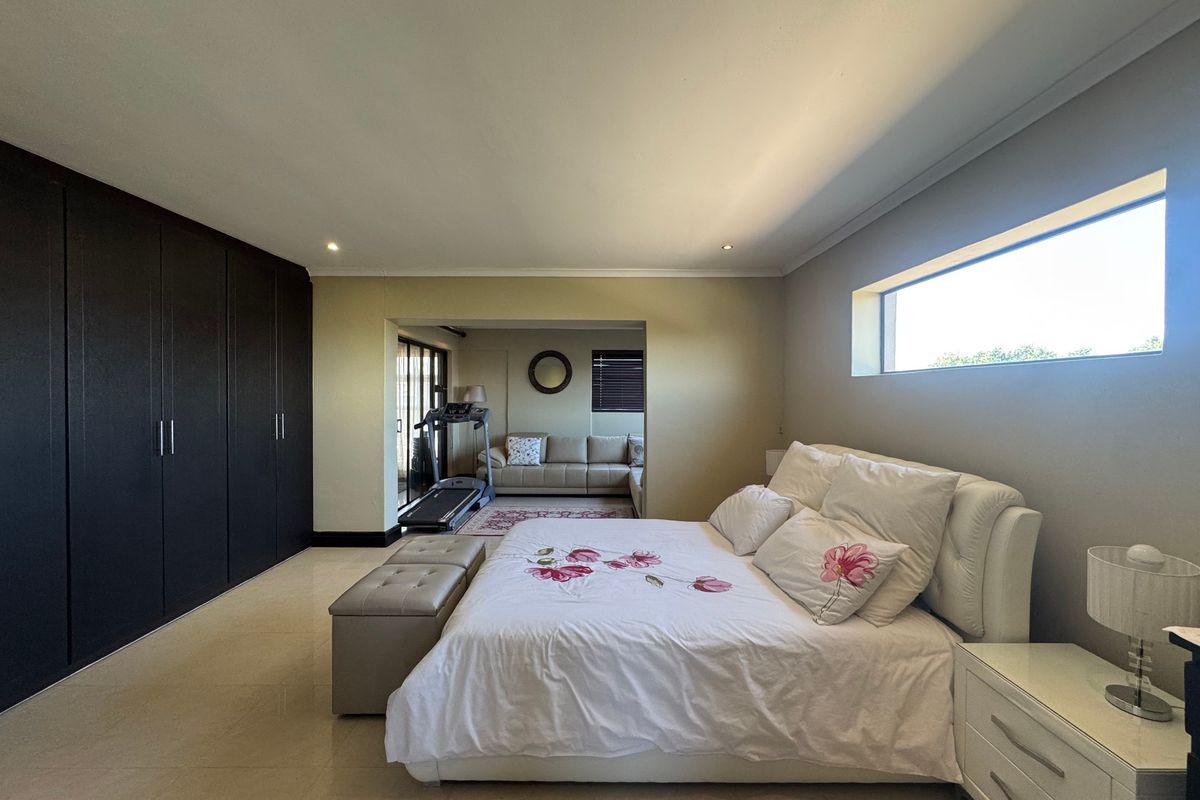 Spacious bedroom featuring extensive built-in cupboards, neutral tiled flooring, and a large horizontal window providing natural light, with an adjoining seating area.
