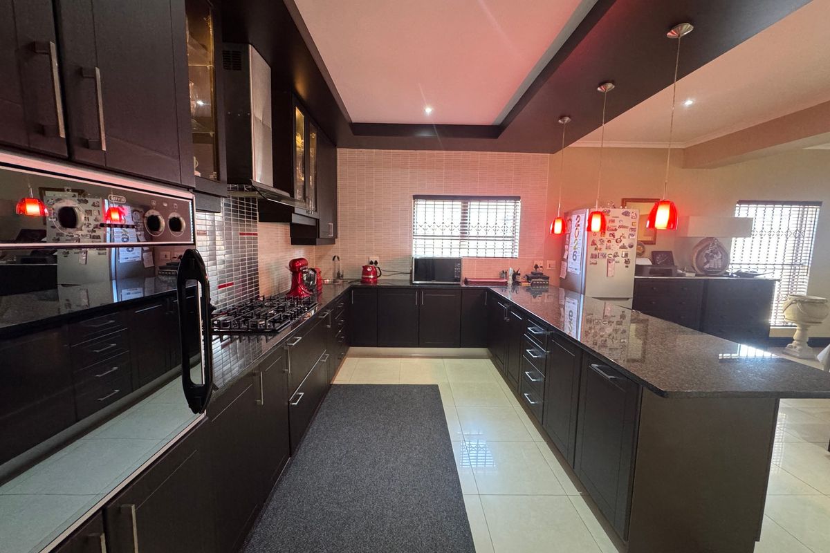 Modern kitchen featuring dark cabinetry, granite countertops, built-in oven, gas hob, and stylish pendant lighting, offering a functional and contemporary cooking space.