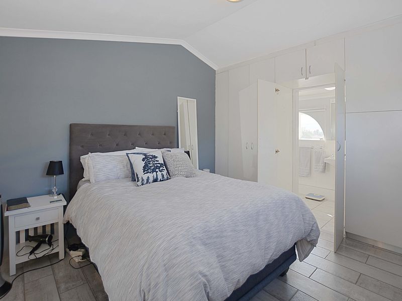 A well-maintained bedroom featuring built-in cupboards, tiled flooring, and a vaulted ceiling, with direct access to an en-suite bathroom.